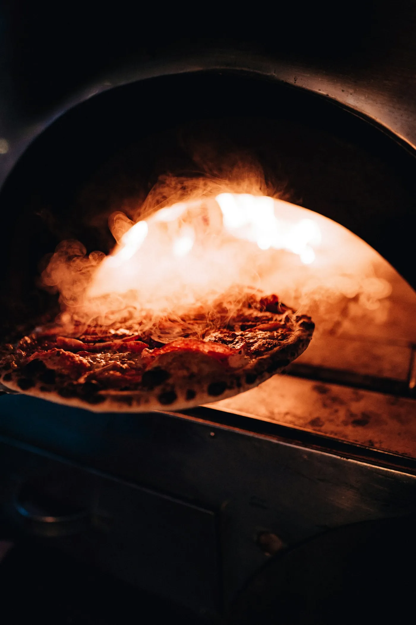 Pizza saliendo del horno en la pala, con humo